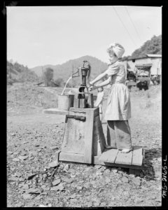 Daughter of a miner getting water at the well which is the only source of approved drinking water in the camp, a... - NARA - 541151