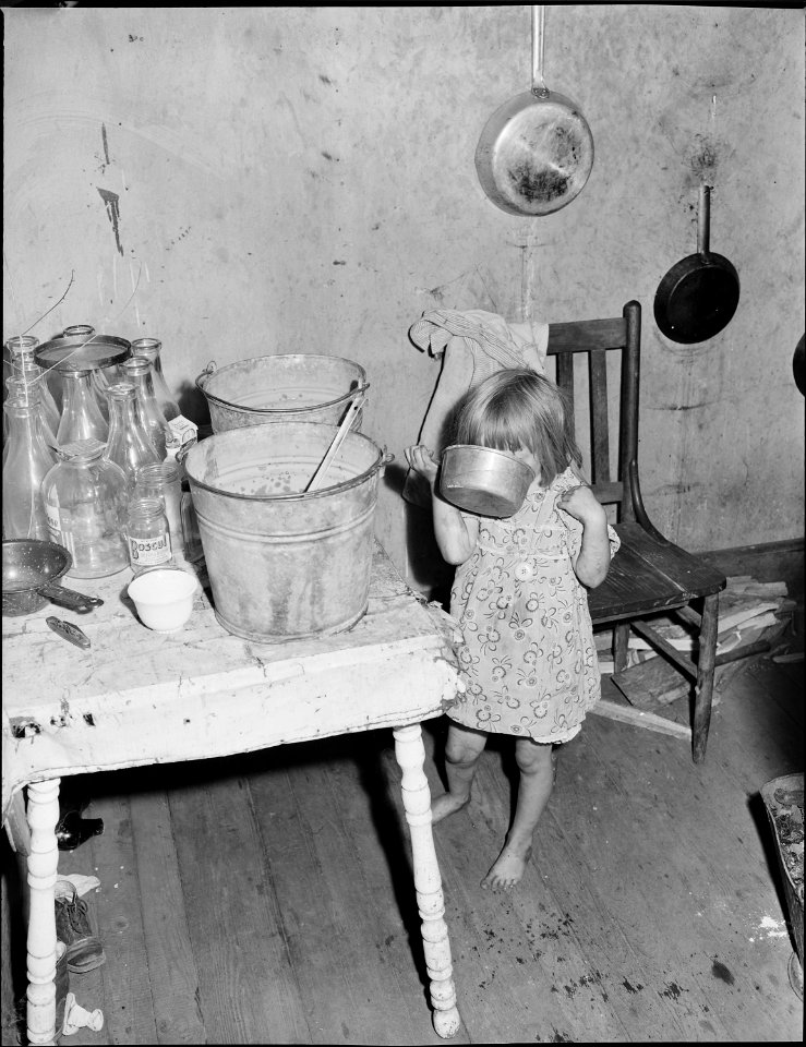 Daughter of Bill Daniels, drinking water. This water was red and thick with iron rust, as much as a quarter inch of... - NARA - 540991