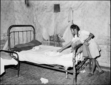 Daughter of Lawson Mayo, disabled miner, makes the bed in the four room house which the two adults and ten children... - NARA - 540970