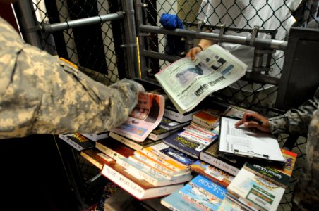 A detainee takes a newspaper given to him from a guard in Camp Five DVIDS368270