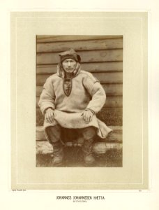 Johannes Johannesen Hætta sitter på en trebenk utenfor bygning - Norsk folkemuseum - NF.15006-070