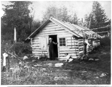 Man with shotgun at doorway of cabin and a deer hanging from pole at camp, Eighth Lake, Fulton Chain, Adirondack Mountains, N.Y. LCCN2003678333