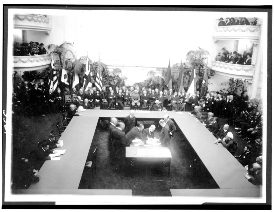 Secty of State Hughes signing the treaties resulting from the Conference of Limitation of Armaments today. Other members of the American delegation around the table LCCN91730757