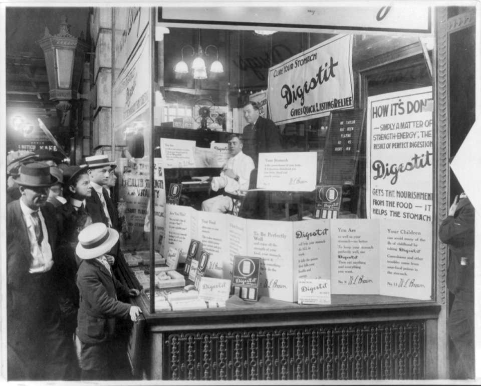 Shoppers looking at window display of Brown's Drug Store, advertising Digestit, a stomach relief patent medicine; product is being endorsed by a pianist, Mr. Thomas, who has been playing LCCN2001706341