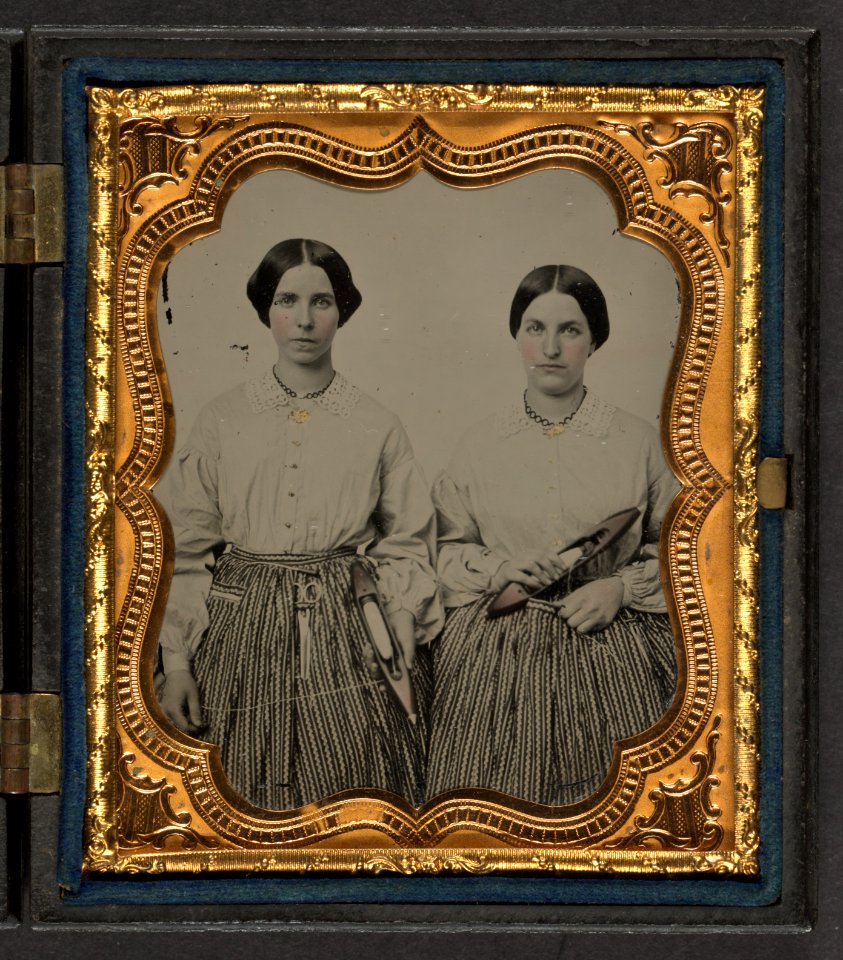 Sisters Lucretia Electa and Louisa Ellen Crossett in identical skirts, blouses, and jewelry with weaving shuttles LCCN2010648856