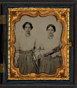 Sisters Lucretia Electa and Louisa Ellen Crossett in identical skirts, blouses, and jewelry with weaving shuttles LCCN2010648856