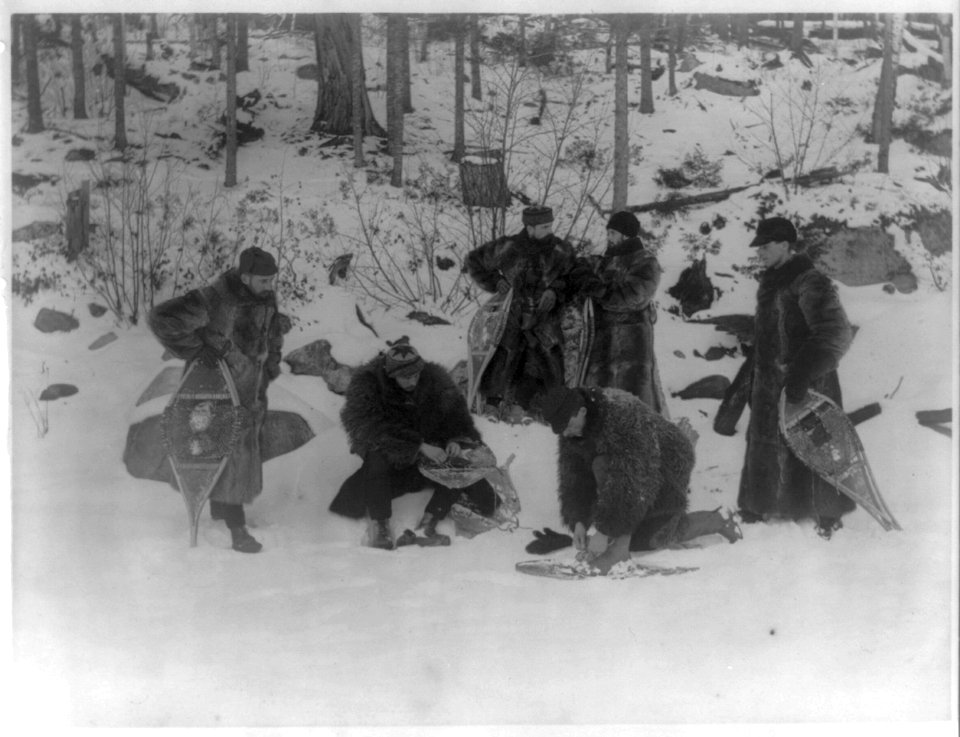 Six men in heavy fur coats putting on snowshoes LCCN2016648156