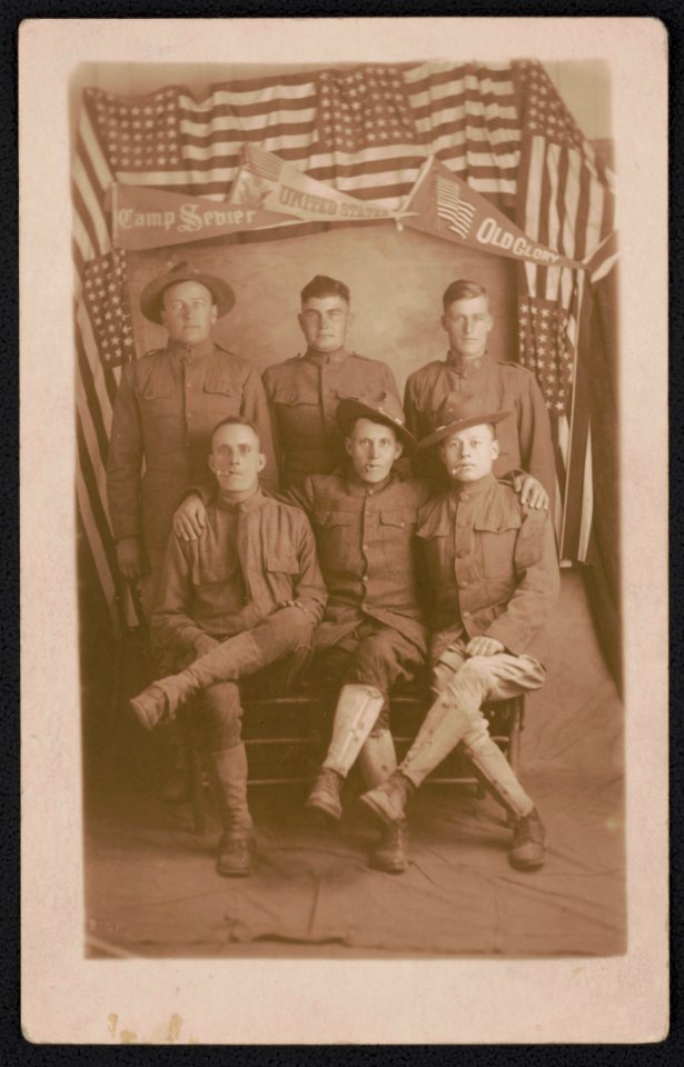 Six unidentified soldiers in front of American flags and pennants for Camp Sevier, United States, and Old Glory LCCN2018645957