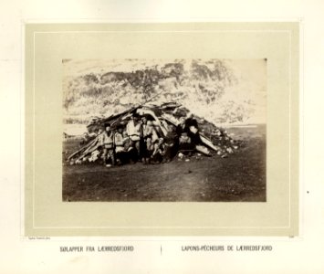 Sjøsamer sitter utenfor gamme i Lerresfjord i Finnmark med fjell i bakgrunnen - Norsk folkemuseum - NF.15006-144