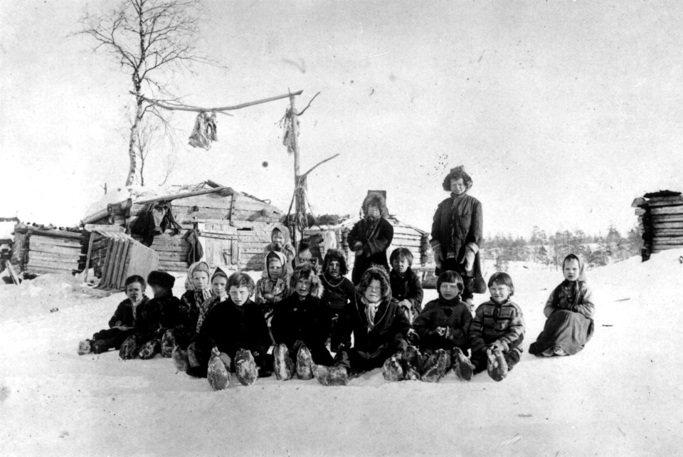 Skoltesamiske skolebarn sitter i snøen ved Pasvik-siidaens skole, Pasvik, Sør-Varanger, Finnmark - Norsk folkemuseum - NF.06725-021