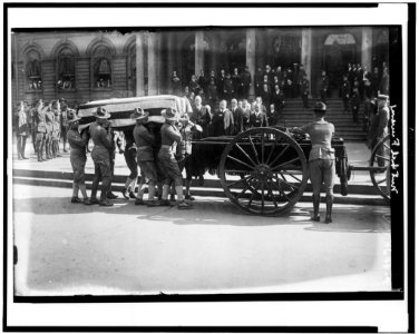 Soldiers loading flag-draped casket of former New York City mayor John Purroy Mitchel onto wagon, with Theodore Roosevelt and other officials holding their hats in respect LCCN91705129