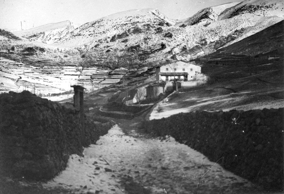 Sortida del poble de Gòsol amb masia i al fons la Serra del Cadí nevada