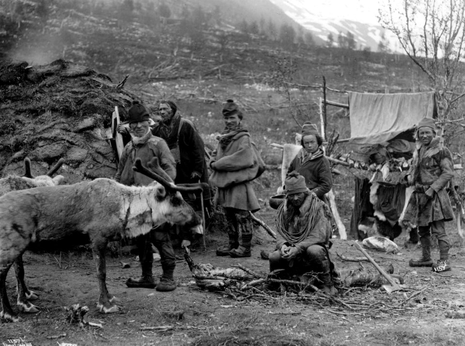Svenske samer, muligens fra Karesuando, foran en gamme, et reinsdyr i forgrunnen - Norsk folkemuseum - NF.06789-018