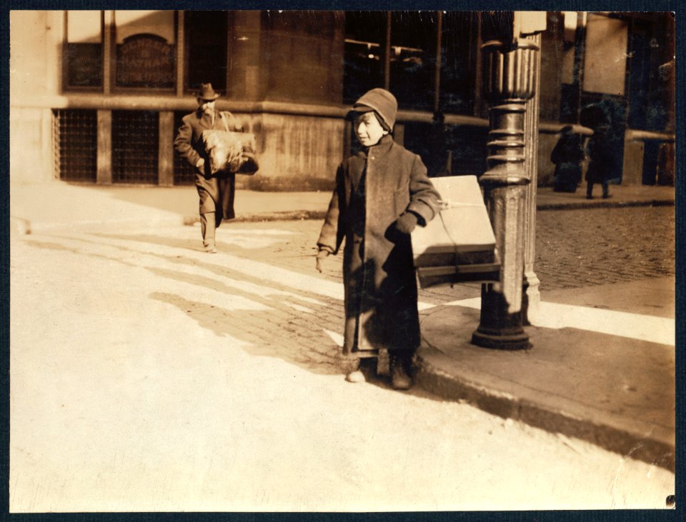 Ten-year-old child carrying a box of artificial leaves from Leroy St. across B'(road)way, New York. LOC nclc.05491
