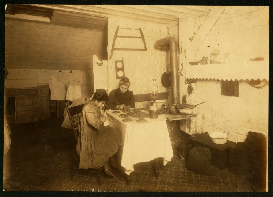 Tessie Sposato, 12 yrs. old girl and her mother picking nuts in attic of tenement, 141 Hudson St., N.Y. She holds the nuts against her dirty apron as she picks them out. Works until 9 p.m. LOC nclc.04093
