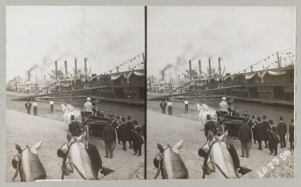 Theodore Roosevelt seated in horse-drawn carriage waving to the public with his hat. Numerous steamboats are docked along the bank LCCN2013651309