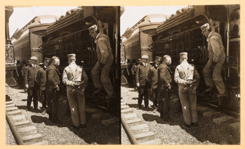 Theodore Roosevelt standing by a railroad car with workers and other men LCCN2009633751