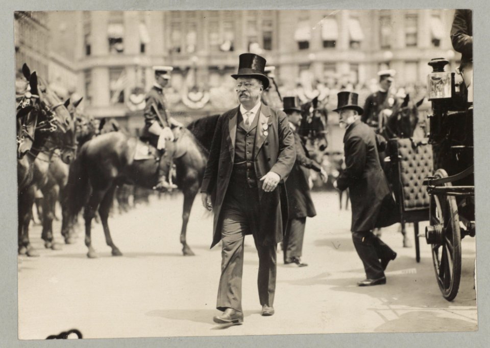 Theodore Roosevelt walking in top hat, tails, and medal; with men, carriage, and horses in background LCCN2010645534