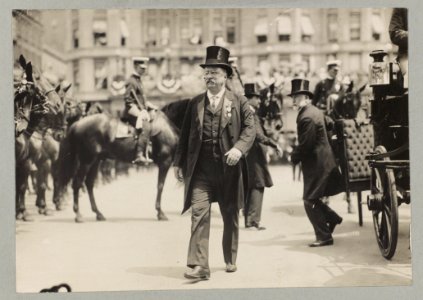 Theodore Roosevelt walking in top hat, tails, and medal; with men, carriage, and horses in background LCCN2010645534