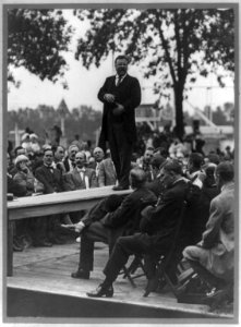 Theodore Roosevelt standing on table outdoors and making speech to men seated around him, hands at waist) - Smith Art Photography, Freeport, Ill LCCN91787239