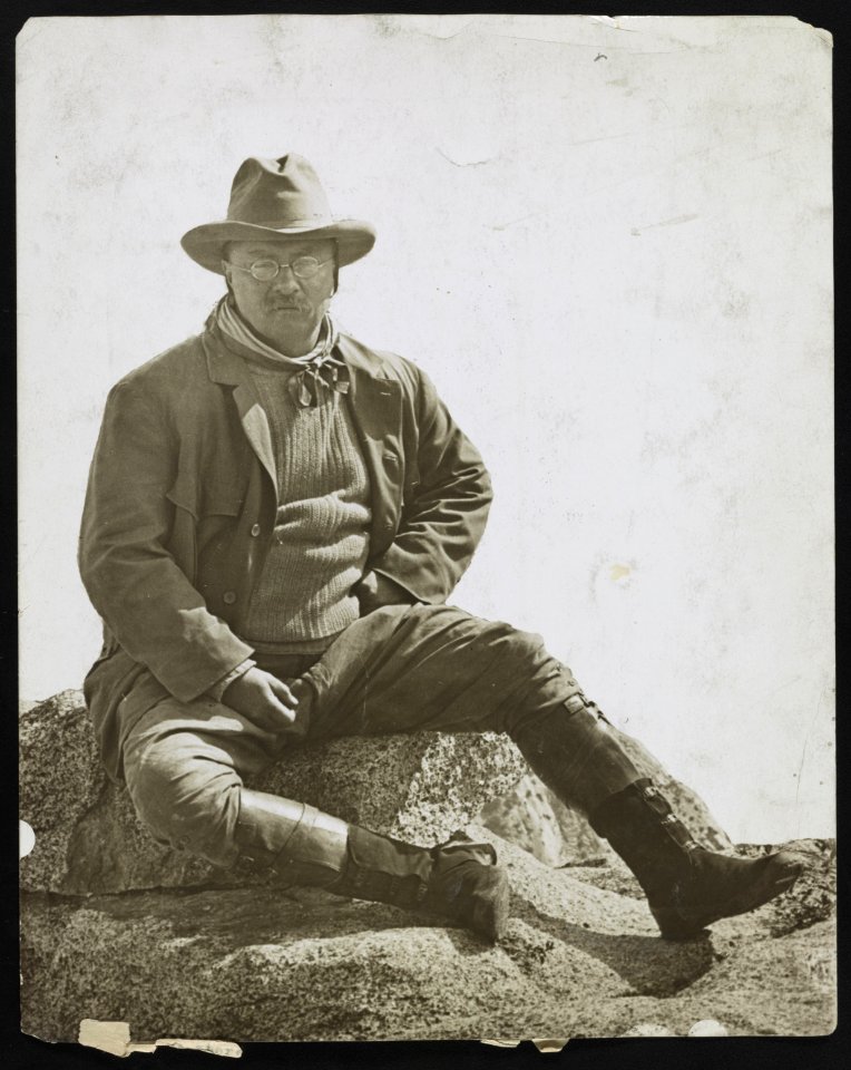 Theodore Roosevelt, sitting on a large stone, at Glacier Point in California LCCN2013650922