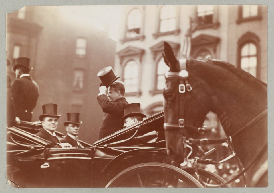 Theodore Roosevelt, standing in an open carriage, tipping his hat to the public LCCN2013651337