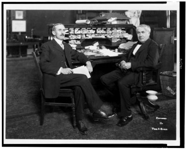 Thomas Alva Edison, full-length portrait, seated at his desk, facing left, with Mr. Wilson LCCN92522141