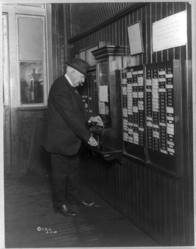 Thomas Alva Edison, 1847-1931, punching time clock on his 74th birthday anniversary, February 11, 1921, standing, rear view LCCN2005687286