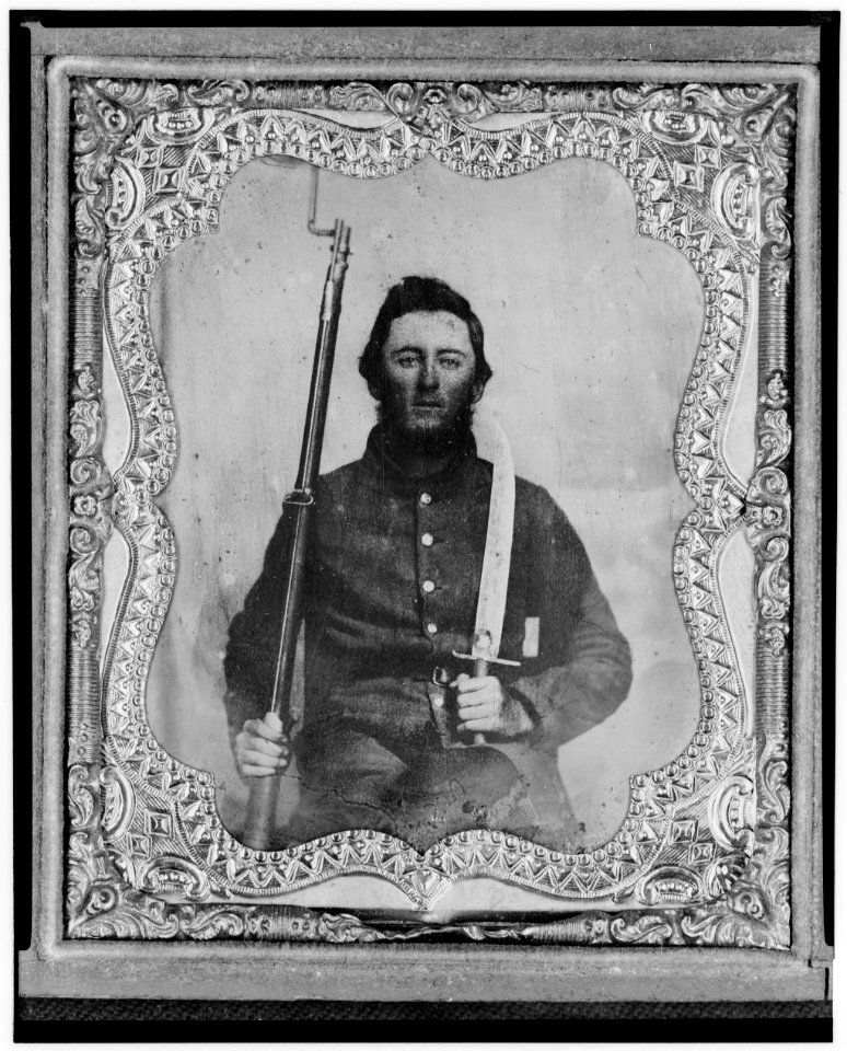 Thomas Kitchen, Pvt., Georgia regiment, C.S.A., three-quarter length portrait, seated holding bayonet and rifle, facing front LCCN2005695738