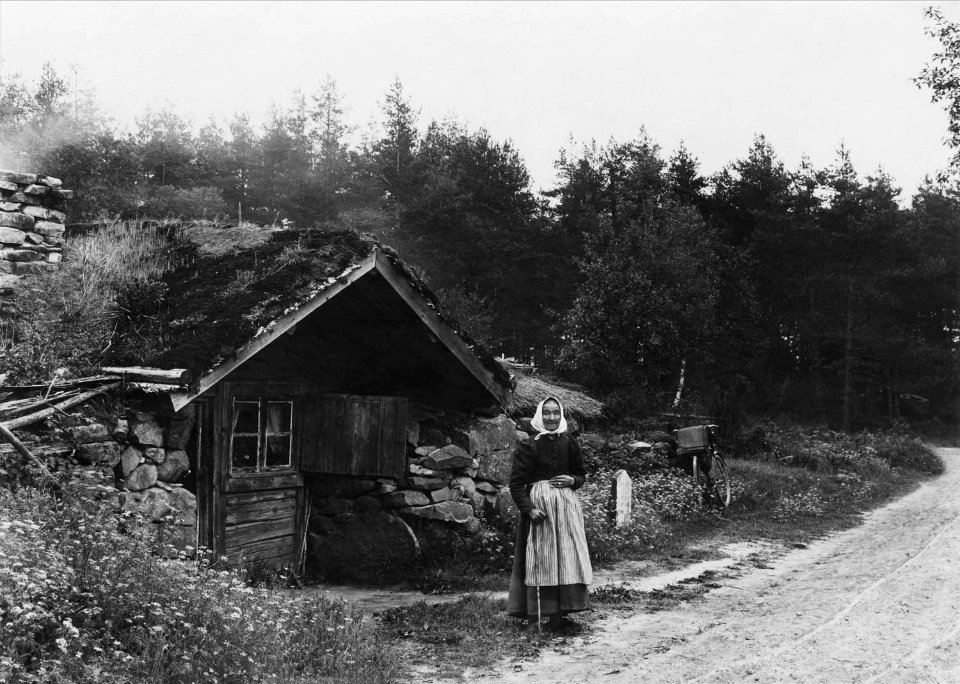 Äldre kvinna framför backstuga (jordstuga) - Nordiska Museet - NMA.0051913