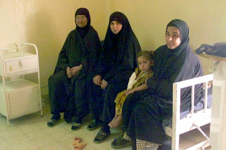 Three Iraqi Women and a small girl sit on an outdated hospital bed while visiting a family member DM-SD-04-04693
