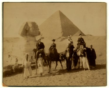 Three women and a man in western attire, seated on camels, several local men stand before the camels holding the reins, a pyramid and the sphinx in background LCCN2004674239