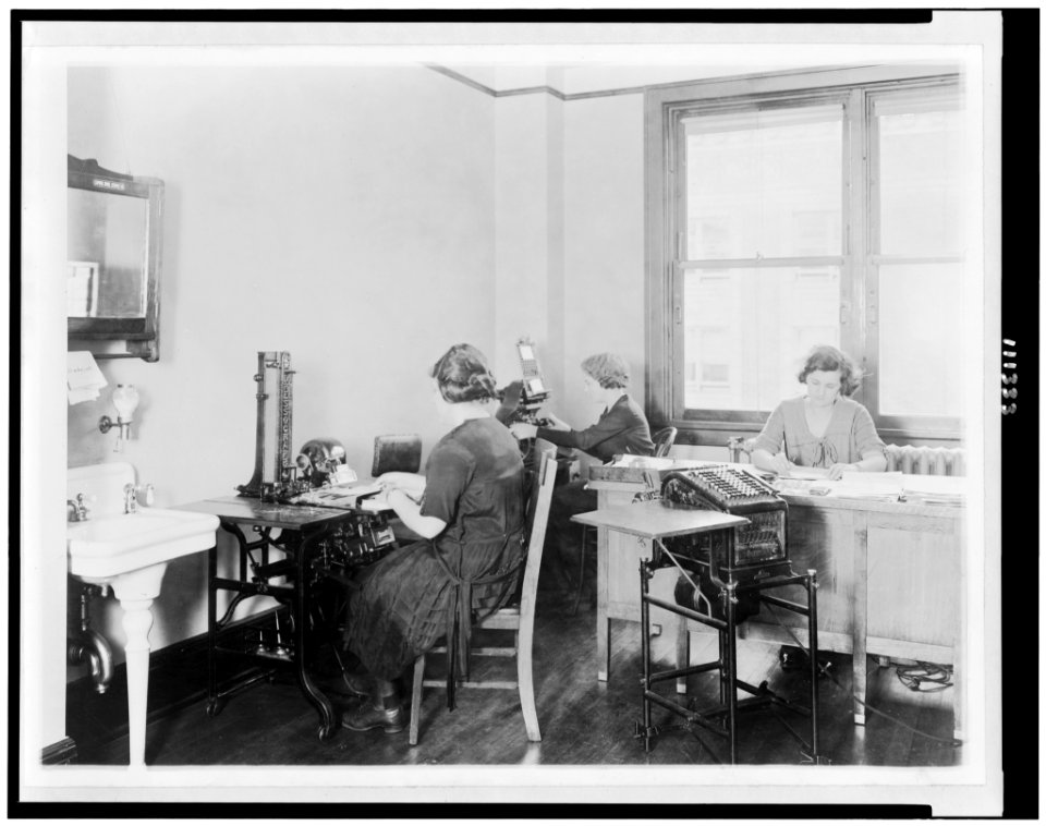 Three young women at work in an unidentified Washington, D.C. office. The girl at the left is operating an addressograph LCCN94507461