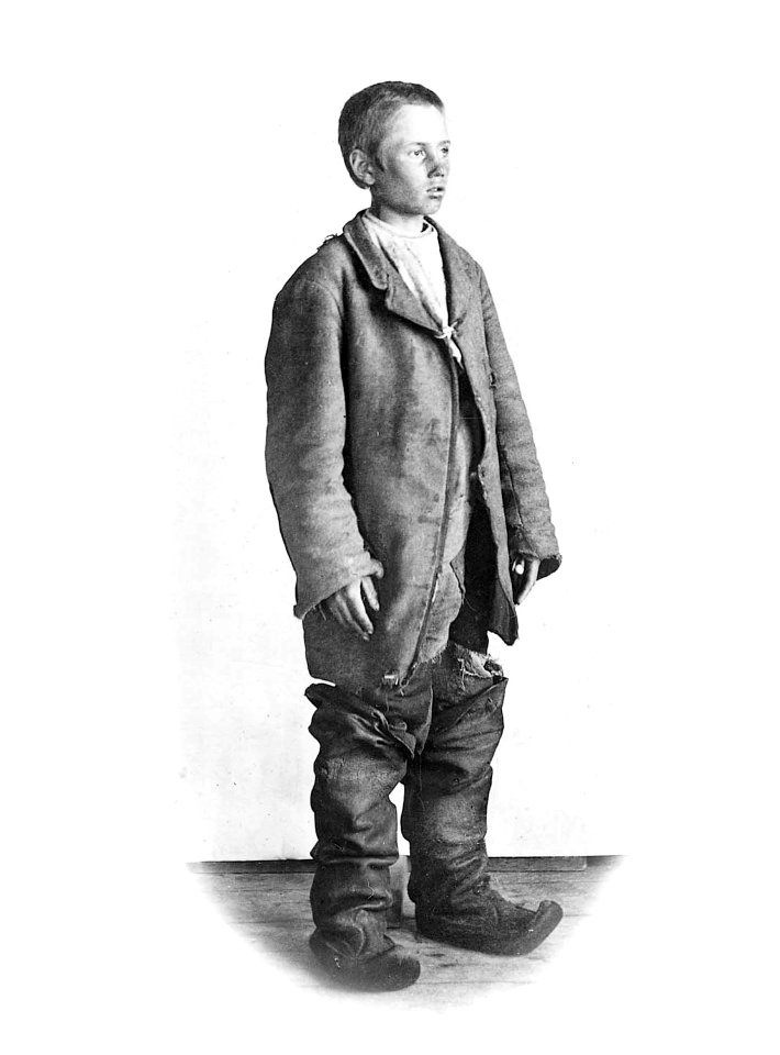 Tiggargosse, ung pojke i för stora, hängande och trasiga kläder och stora, höga stövlar i Lappträsk, 1902 - Nordiska Museet - NMA.0052712