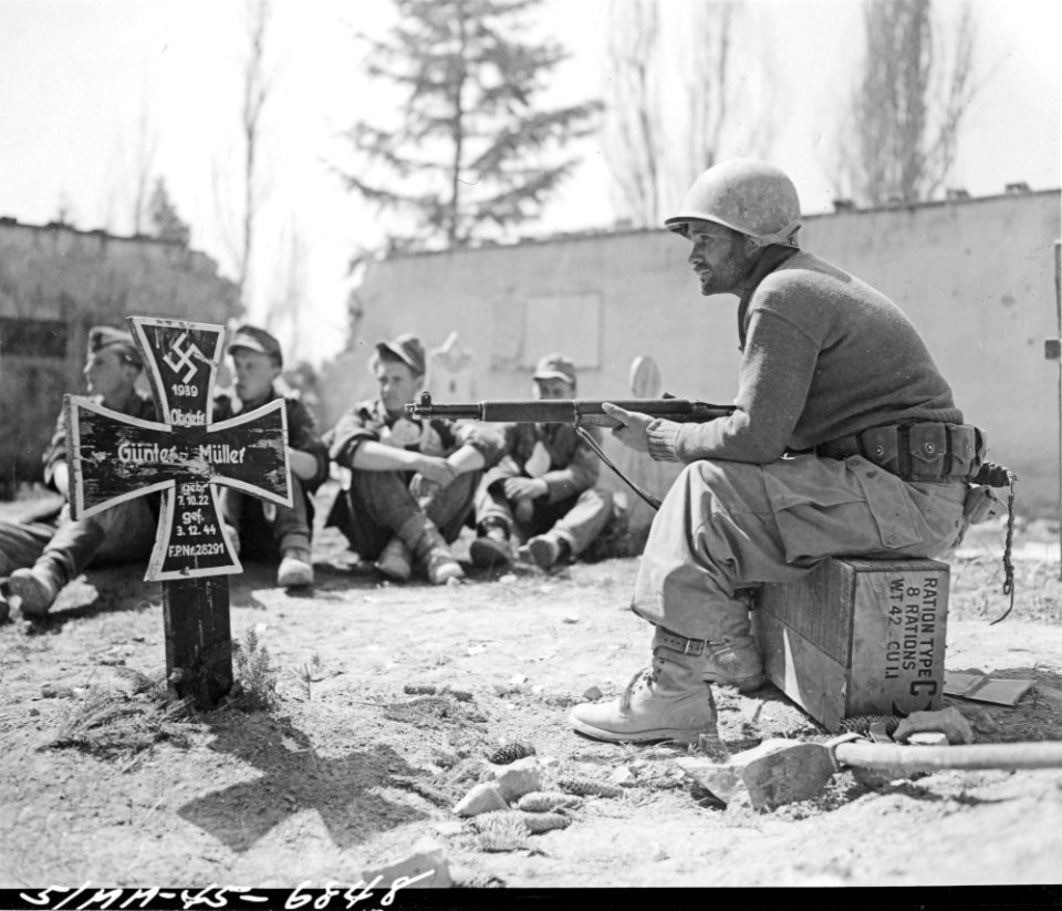 Tired and dirty from three days of hard fighting, Pvt. Odell J. Farr of Company 'F', 2nd Battalion, 87th Regiment, 10th Mountain Division, guards German prisoners in an Italian cemetery in Suzzano, Italy
