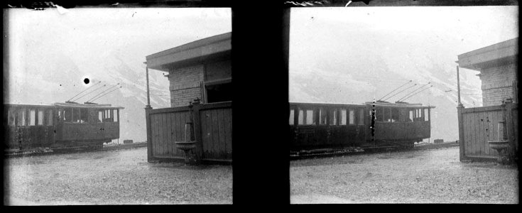 Tren al costat d'un edifici amb una font i muntanyes al fons