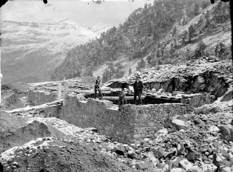 Tres homes a les obres de construcció del refugi de la Renclusa i al fons muntanyes nevades