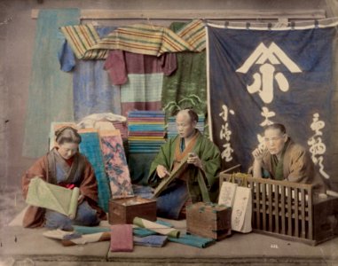 Trois personnages devant un étalage de tissus