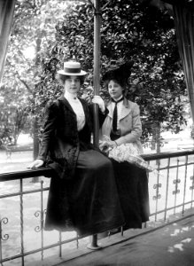 Två unga kvinnor i dräkt och hatt sittande på räcke - Nordiska Museet - NMA.0054263 photo