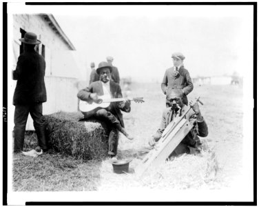Two Afro-American men, outside of stable, with Kazoos in their mouths, one of them seated on haybale and playing guitar, the other playing homemade string instrument, Washington, D.C. or New LCCN93507058