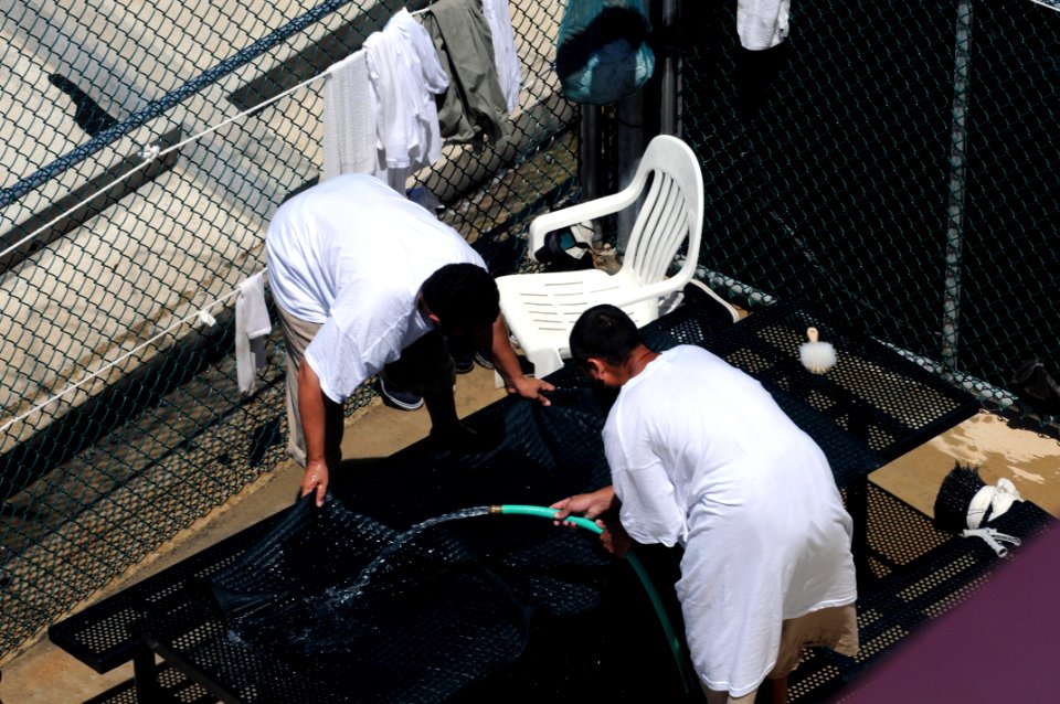Two detainees wash a mat in the outdoor recreation area of Camp Six at Joint Task Force Guantanamo DVIDS380254