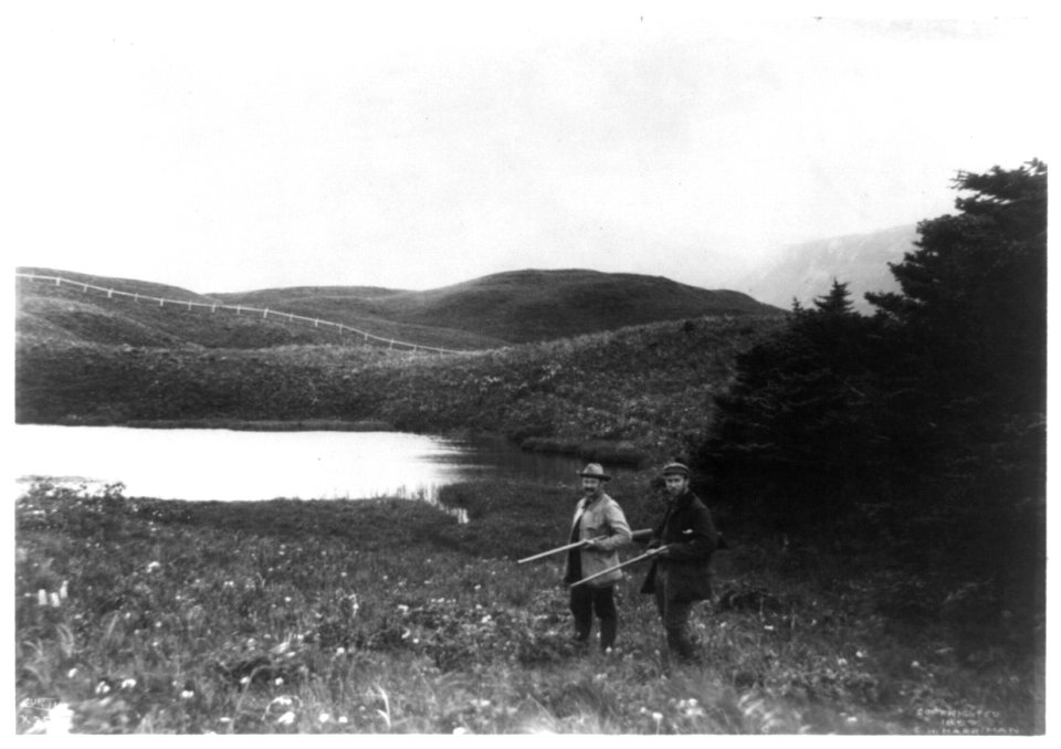 Two men with guns in foreground, pond and mountain in background, taken during the Harriman Alaska Expedition, 1899 LCCN92513833