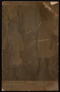 Two young girls, wearing dresses, standing on porch LCCN2015649995