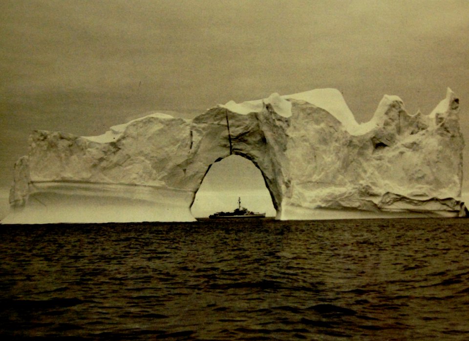 U.S. Coast Guard Cutter Eastwind (WAGB-279) seen through a natural arch in an iceberg, 1952 (21436454424)