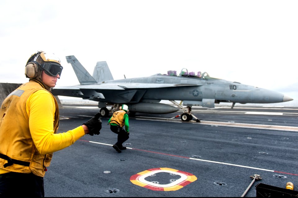 U.S. Navy Aviation Boatswain's Mate (Handling) 2nd Class Christopher O'Neil, foreground, directs an F-A-18F Super Hornet aircraft assigned to Strike Fighter Squadron (VFA) 32 onto a catapult on the flight deck 140926-N-ZG705-349