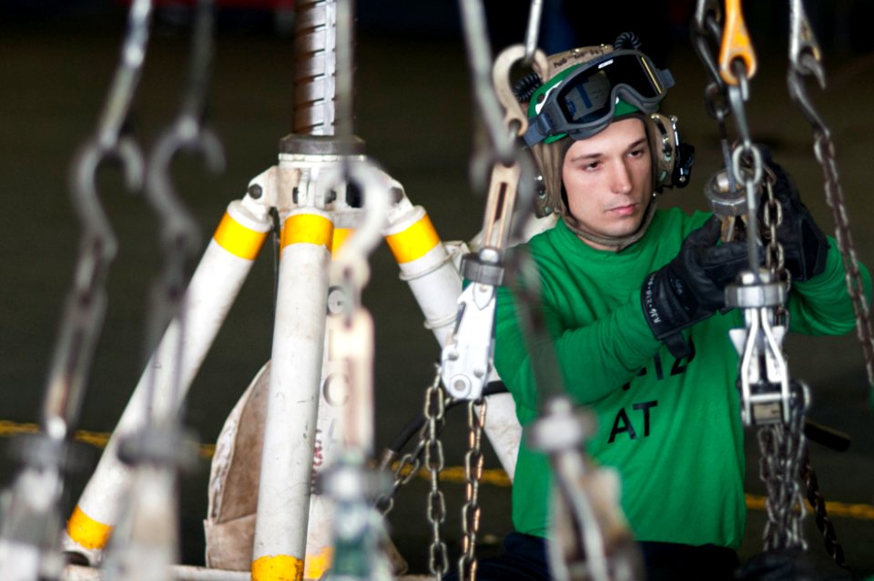 U.S. Navy Aviation Electronics Technician 3rd Class Zachariah Roberts, assigned to Airborne Early Warning Squadron (VAW) 126, maintains slack on tie-down chains while an E-2C Hawkeye aircraft is lifted on jacks 140118-N-ZG705-020