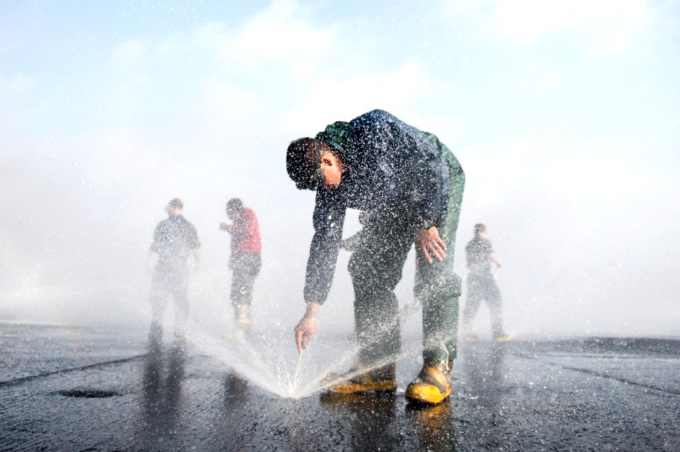 U.S. Navy Aviation Boatswain's Mate (Handling) Airman Anthony Whitley, foreground, clears debris from a countermeasure washdown sprinkler on the flight deck of the aircraft carrier USS Harry S. Truman (CVN 75) 140316-N-ZG705-210