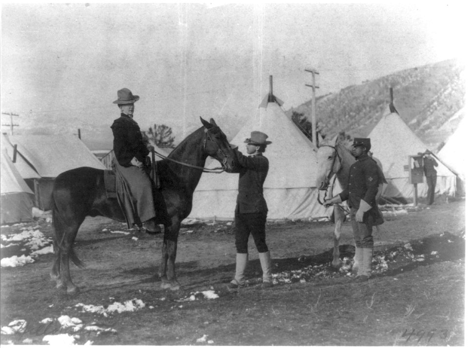 U.S. soldier-guide holding woman's horse, African American trooper alongside, tents in background, Yellowstone Park, Wyo. LCCN2016649445