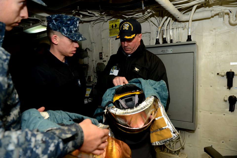 U.S. Navy Capt. Frank Dowd, a senior aviation inspector with the Board of Inspection and Survey (INSURV), inspects a crash and salvage helmet with Sailors aboard the amphibious transport dock ship USS Mesa Verde 140116-N-BD629-037