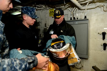 U.S. Navy Capt. Frank Dowd, a senior aviation inspector with the Board of Inspection and Survey (INSURV), inspects a crash and salvage helmet with Sailors aboard the amphibious transport dock ship USS Mesa Verde 140116-N-BD629-037